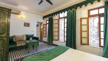 Una habitación con cama, sofá, una mesita, ventilador de techo y ventanas con diseño.