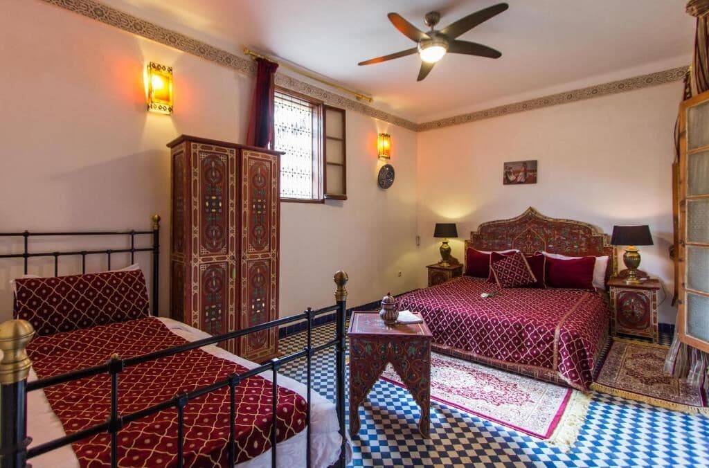 A traditional room with a bed, a wardrobe, a ceiling fan, and patterned rugs.