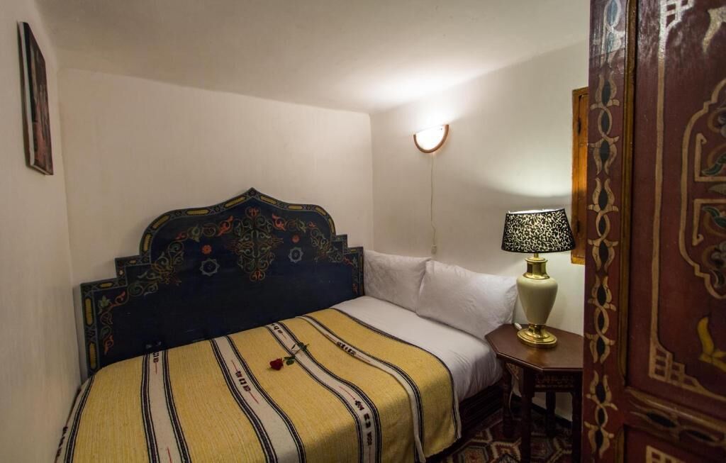 A bedroom with a bed, a bedside lamp, a wall-mounted light, and a patterned rug.