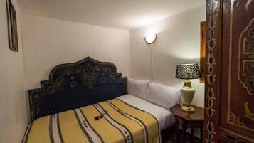 A bedroom with a bed, a bedside lamp, a wall-mounted light, and a patterned rug.