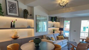 Ein modernes Wohnzimmer mit einem runden Tisch, gelben Stühlen, einer Couch mit gemusterten Kissen und einem großen Spiegel.