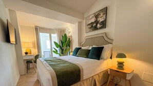 Ein Schlafzimmer mit Bett, Nachttisch, Lampe, Stuhl, Schreibtisch und einer Pflanze.