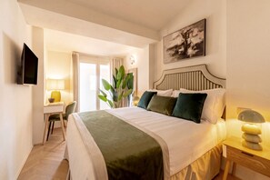 Une chambre d’hôtel comprenant un lit, une table de chevet, une lampe, une télévision, un bureau, une chaise et une grande fenêtre avec des rideaux.