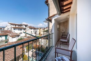 Ein Balkon mit Blick auf eine Stadt, eine kleine Sitzecke und ein Fenster mit einer Zeitung.