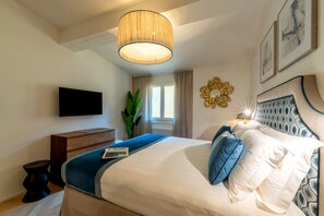 Ein modernes Schlafzimmer mit einem großen Bett, einem Flachbildfernseher, einer hölzernen Kommode und einem Topfpflanze.