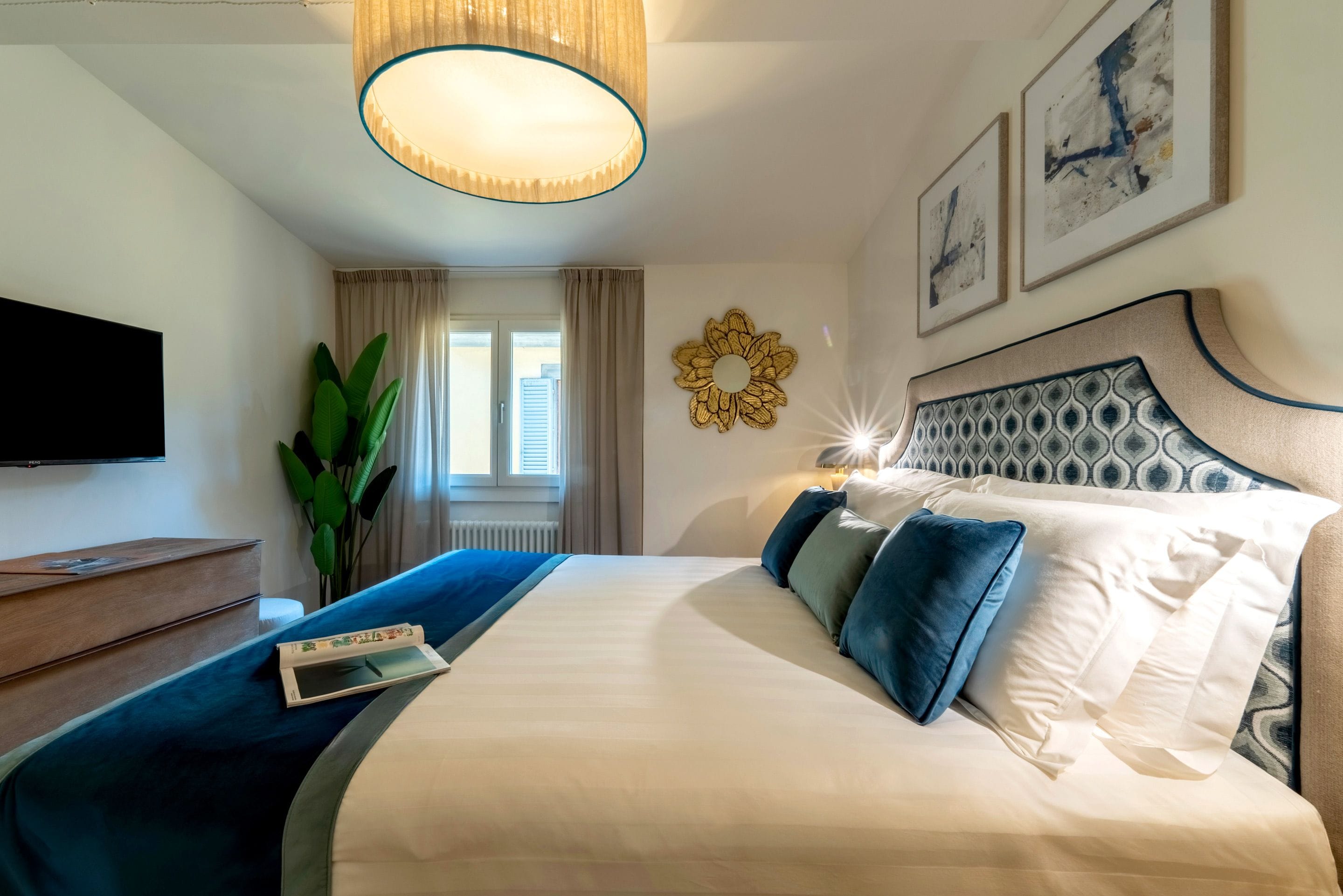 Ein Hotelzimmer mit einem großen Bett, einem Fernseher, einer Pflanze und Kunstwerken an den Wänden.