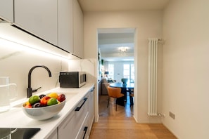 Une cuisine moderne avec un plan de travail blanc, un saladier de fruits et un four à micro-ondes.