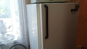 A white refrigerator with a microwave on top, a chair, and a window with lace curtains. - 2-bedroom apartment in lovely Ventspils with air conditioning 1 (Ventspils)