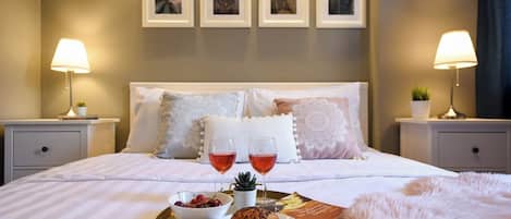 A neatly made bed with a tray of food and drinks, two bedside lamps, and framed pictures on the wall.