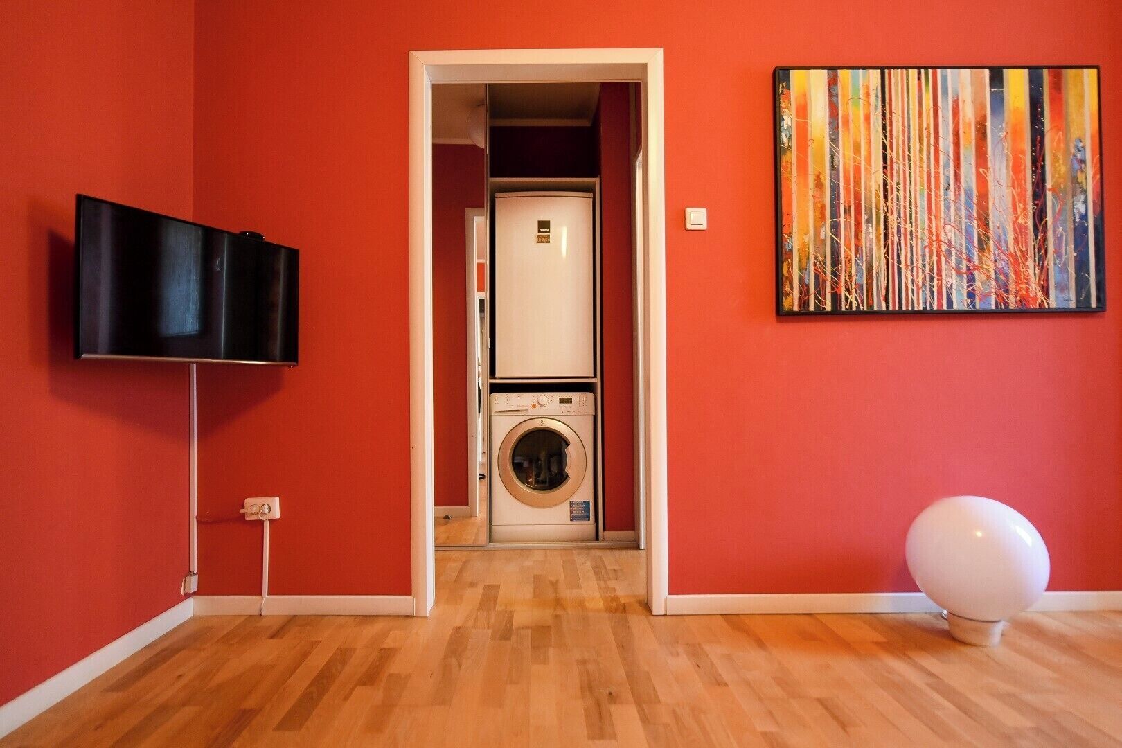 A room with a television, a washing machine, and a painting on the wall.
