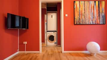 A room with a television, a washing machine, and a painting on the wall.