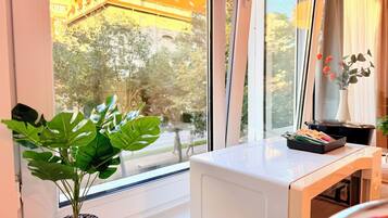 A room with a large window, a potted plant, a table with a black tray, and a vase with flowers.