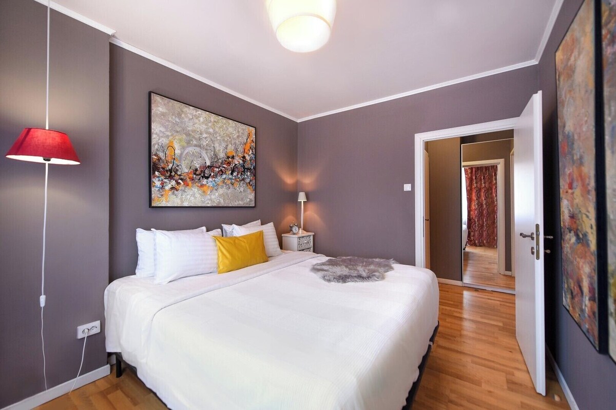 Ein Schlafzimmer mit einem Bett, einer roten Lampe, einem Gemälde und einer Tür zu einem anderen Raum.