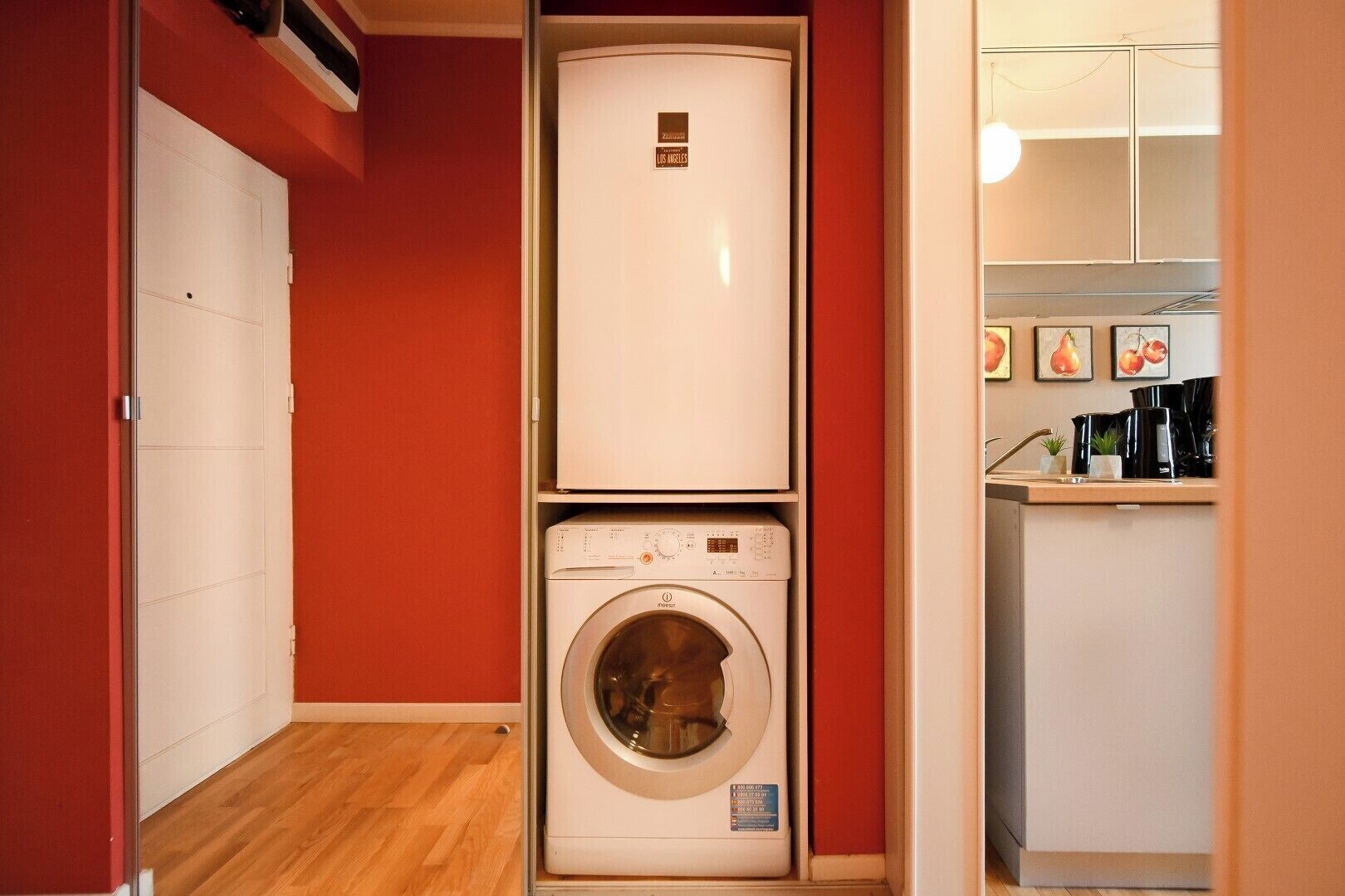 Un espacio compacto con lavadora y secadora, una kitchenette con pileta y cafetera, y una puerta que da a otra habitación.