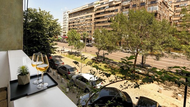 Een balkon met uitzicht op een meerhoog gebouw, geparkeerde auto's en bomen.