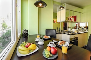 Ein Frühstückstisch mit Früchten, Kaffee und Saft in einem Zimmer mit Fenster, Stuhl und Küchenzeile.