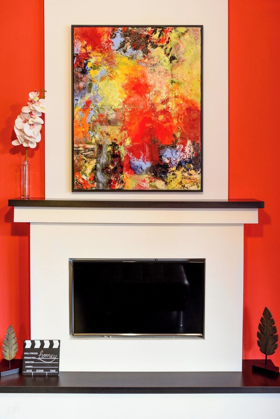 Un tableau abstrait encadré est accroché au-dessus d’une cheminée, et un clap de cinéma est placé en dessous.