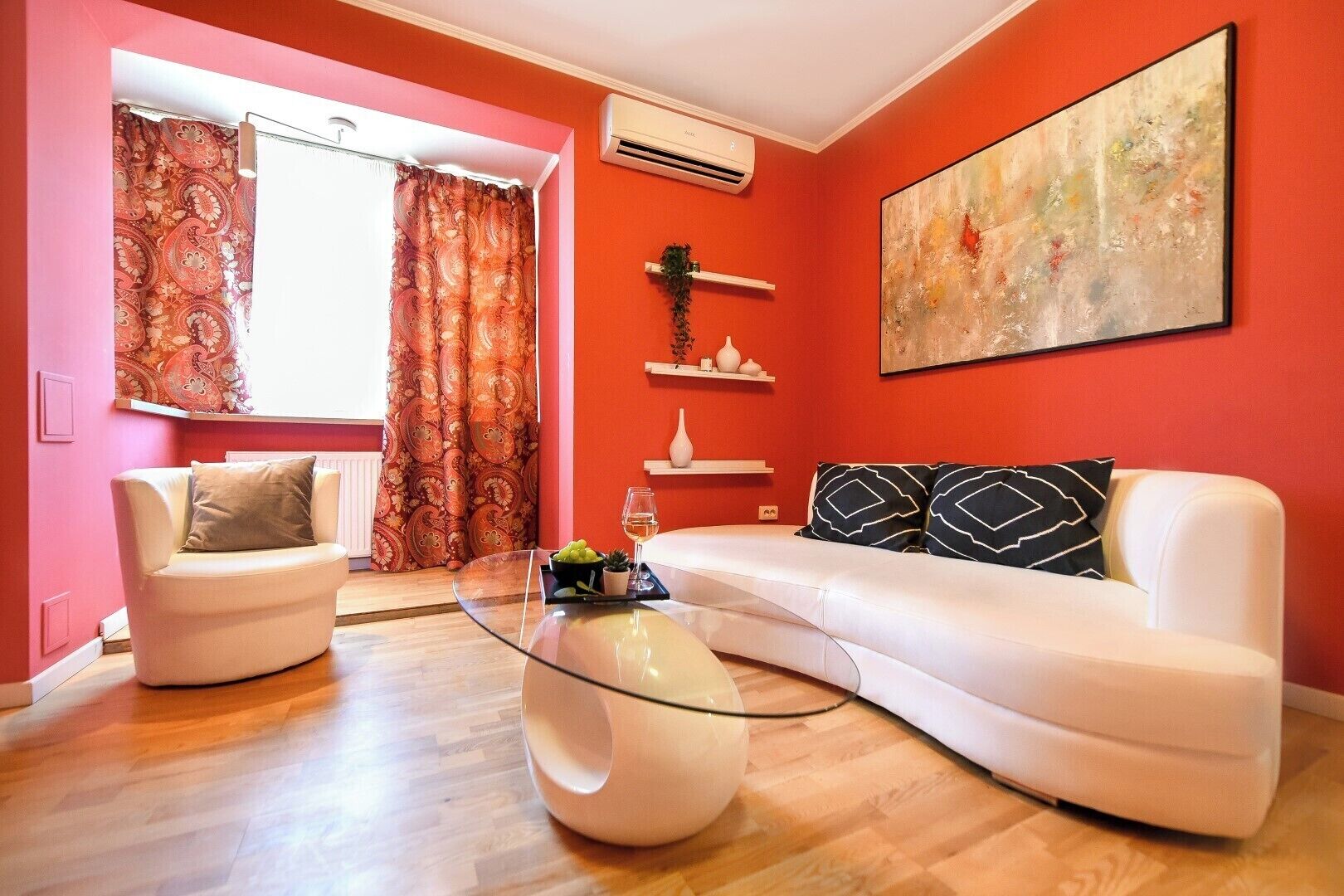 A living room with a white sofa, a glass coffee table, and a red accent wall.