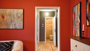 Een kamer met houten vloer, een bed met een zwart-wit kussen, een witte dressoir en een badkamer zichtbaar door een open deur.