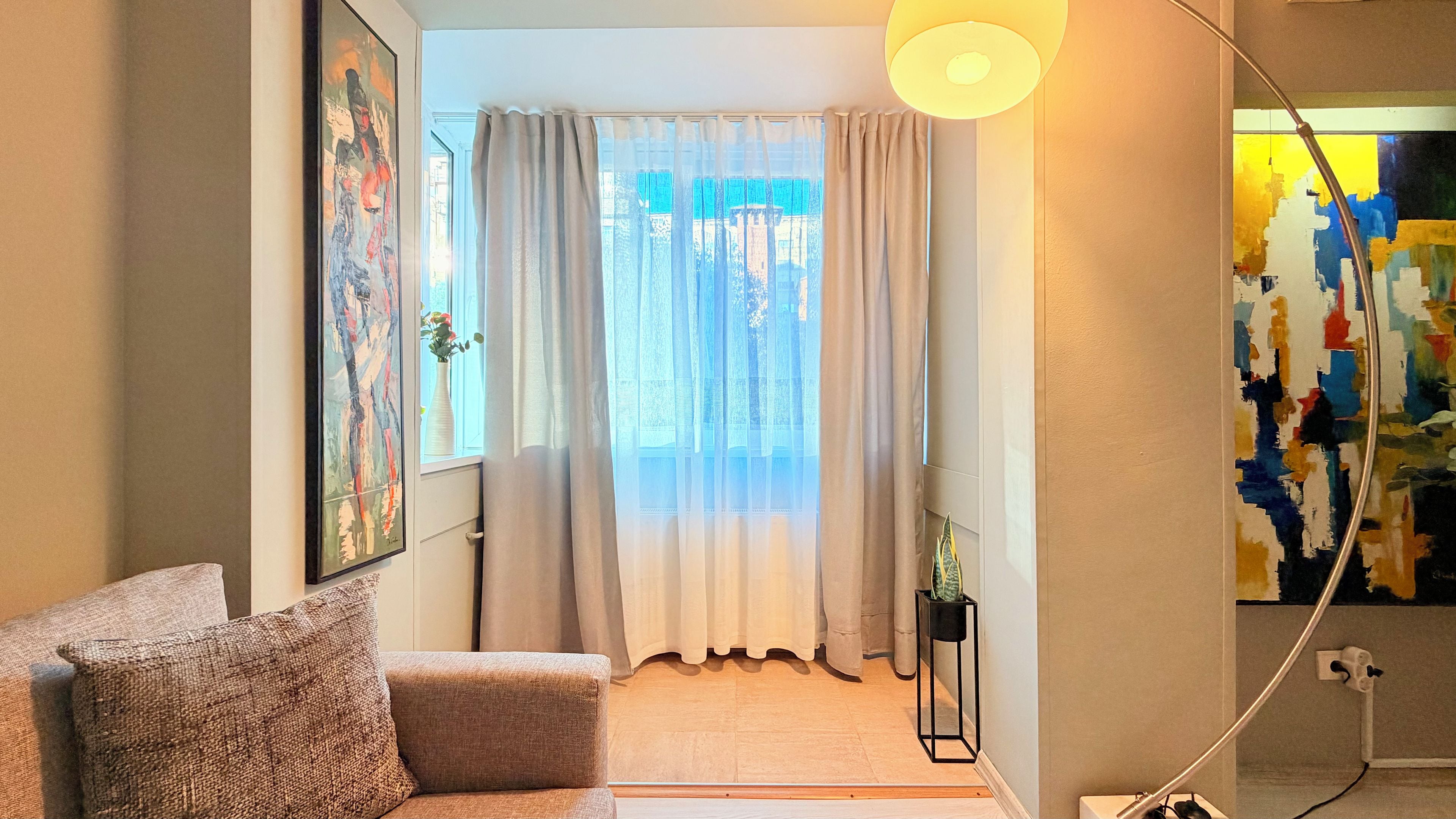 Habitació amb un sofà, una finestra amb cortines lleugeres, un quadre a la paret i una làmpada.