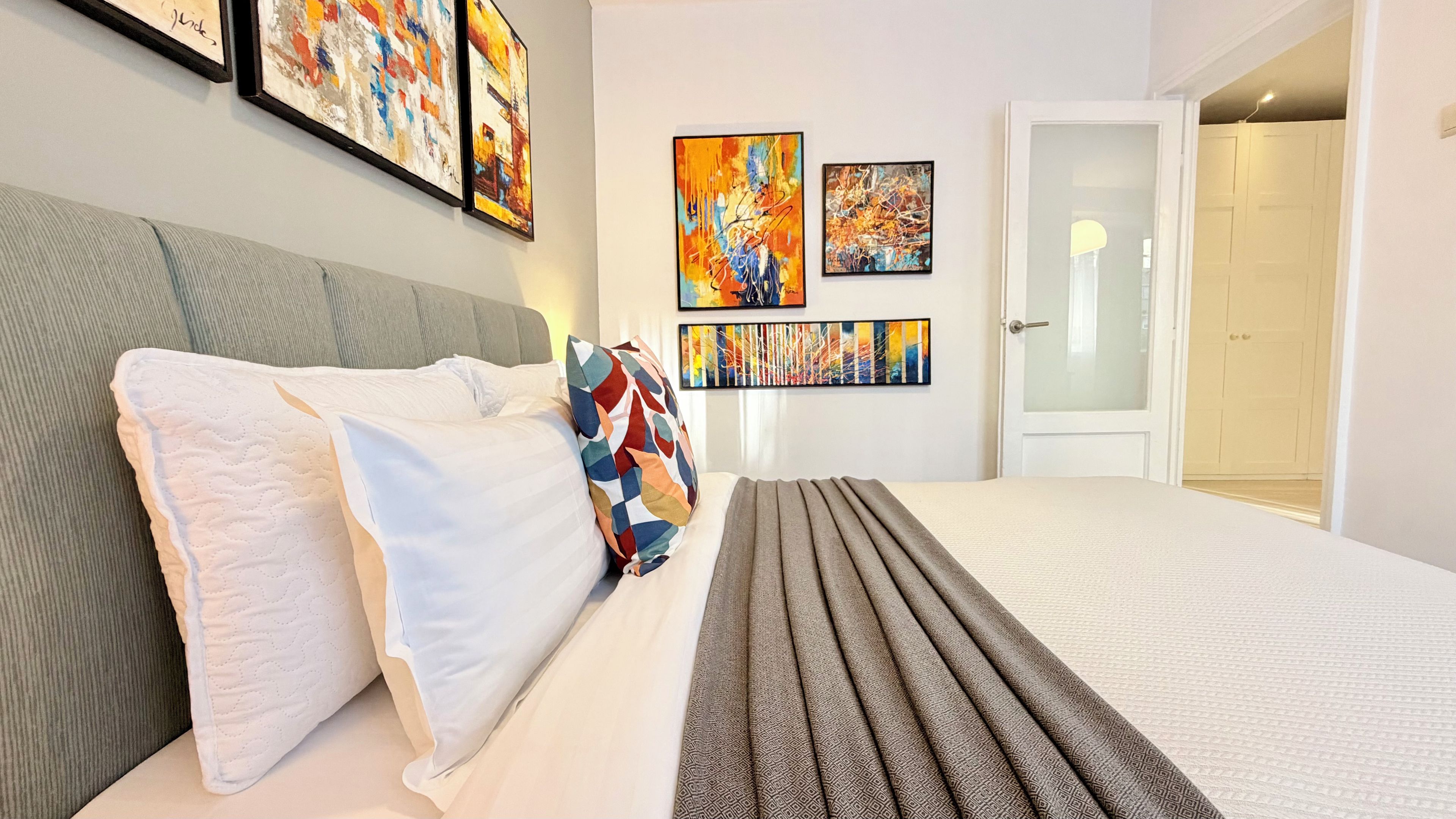 Habitació d'hotel amb un llit, almoines, una manta i una obra d'art abstracta a la paret.
