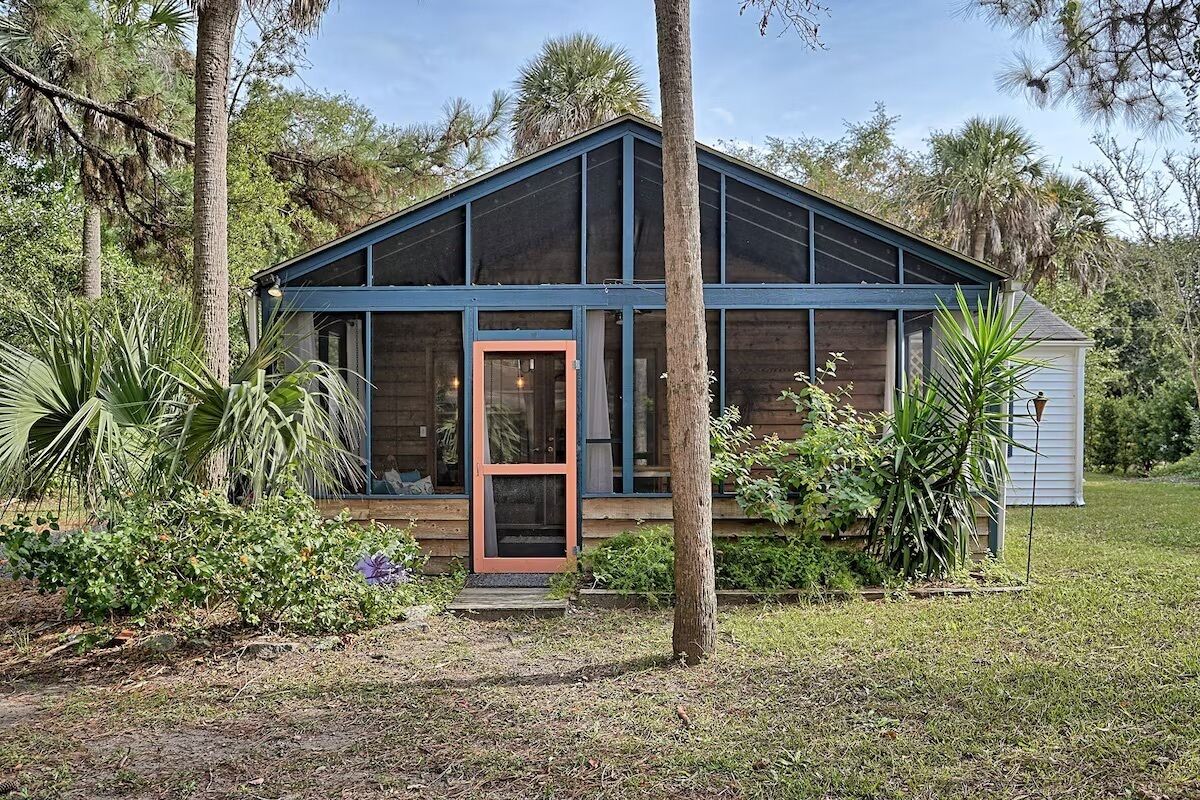 A wooden cabin with a glass front, surrounded by trees and vegetation.