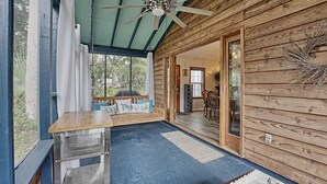 Une cabane en bois dotée d’un ventilateur de plafond, d’un coin repas avec une table et des chaises, et offrant une vue sur l’extérieur grâce à une grande fenêtre.