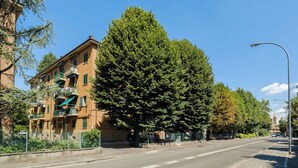 Een meerlaags gebouw met balkons, een heldere lucht en een straat met een geparkeerde auto.