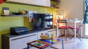 Een moderne woonkamer met een flatscreen-televisie, een printer, een klein tafeltje met een tijdschrift en een opklapbare stoel.