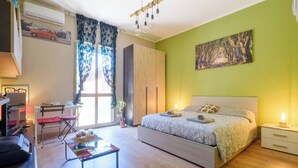 Een slaapkamer met een bed, nachtkastje, bureau, stoel en een raam met gordijnen.
