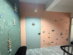 Ein Zimmer mit einer türkisblauen Tür, einer Wand mit Meeresdekorationen, einem Holzbild und einem schwarzen Stuhl.