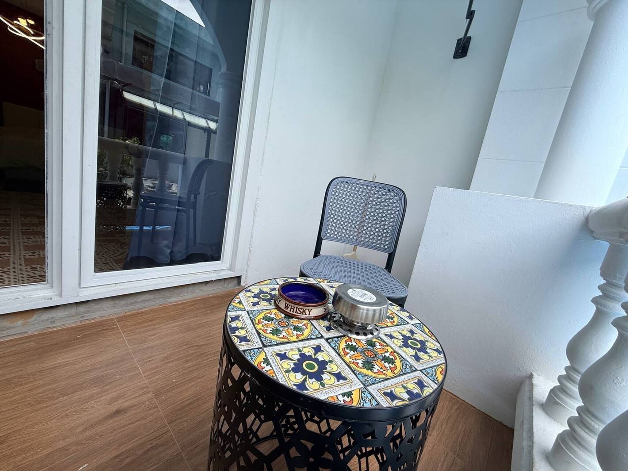 A small round table with a colorful tile top, a chair, and a whisky glass on the table.