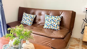 A brown leather sofa with two patterned pillows, a small table with a decorative plant and a dog-shaped container, and patterned floor tiles.