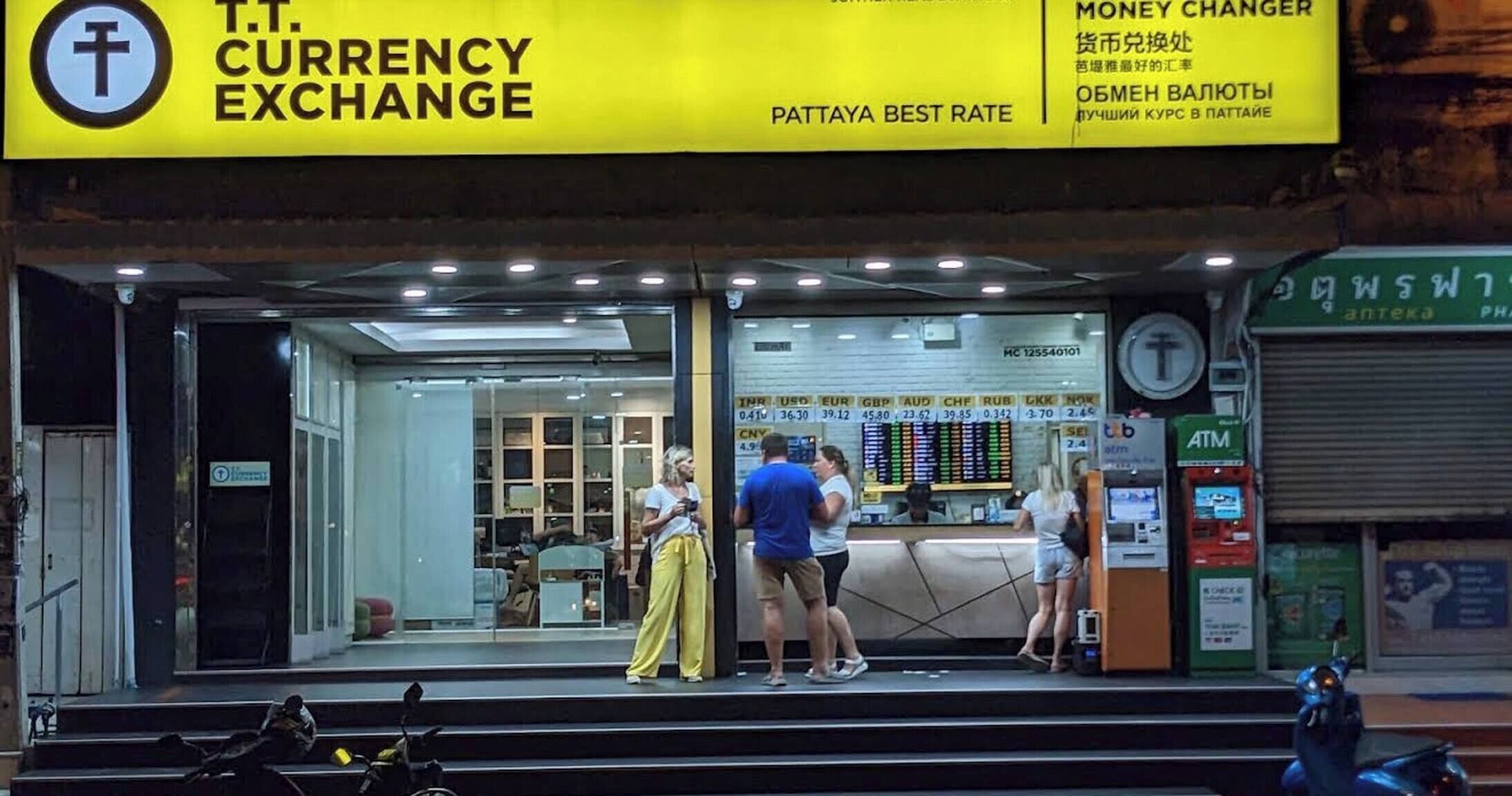 A currency exchange booth with a bright yellow sign, a glass display case, and a few people standing outside.