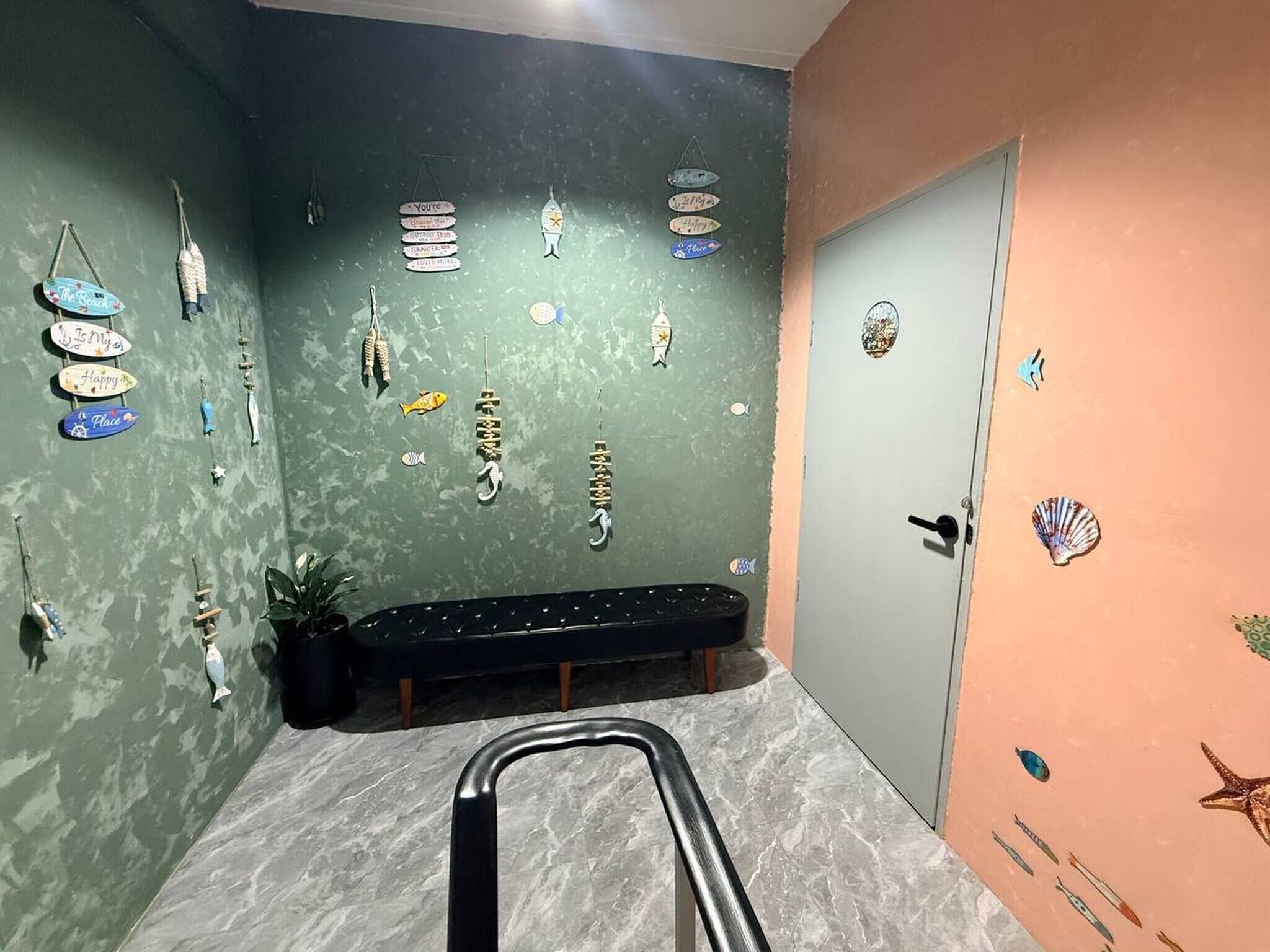 Quarto com parede verde decorada com diversos peixes e objetos com tema marítimo, um banco e uma porta com decoração de estrela-do-mar.