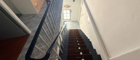 A staircase with a handrail, a dining area with chairs and a table, and a wall with a light fixture.