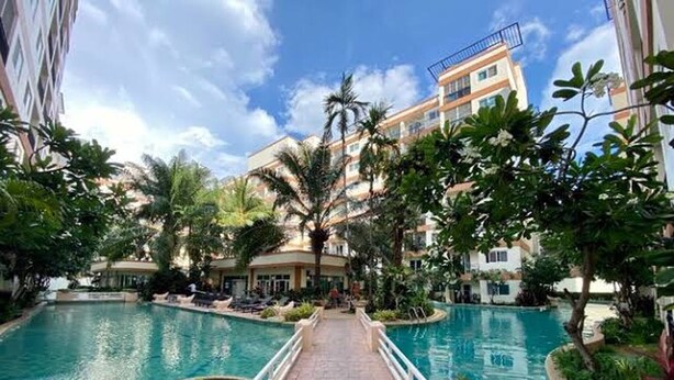 En hotelgård med en central swimmingpool, omgivet af palmer og bygninger.
