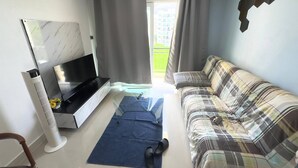 En moderne stue med et fladskærms-tv, en sofa, et sofabord og et stort vindue med gardiner.