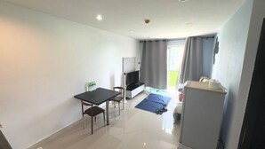 Et hotelværelse med en seng, et fjernsyn, et skrivebord med stol, et lille bord med flasker og et køleskab.