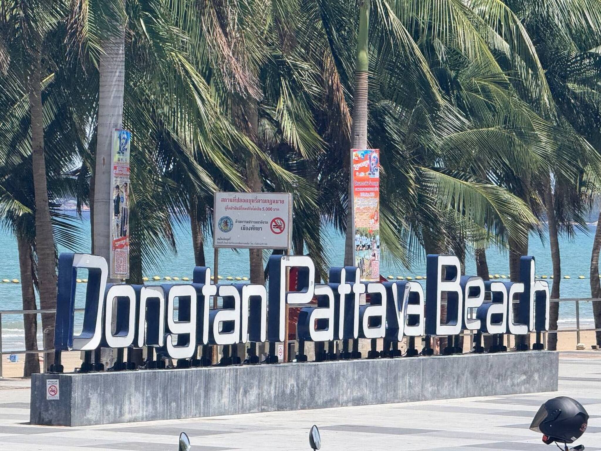 A sign for Dongian Pattaya Beach with palm trees and a beach in the background.