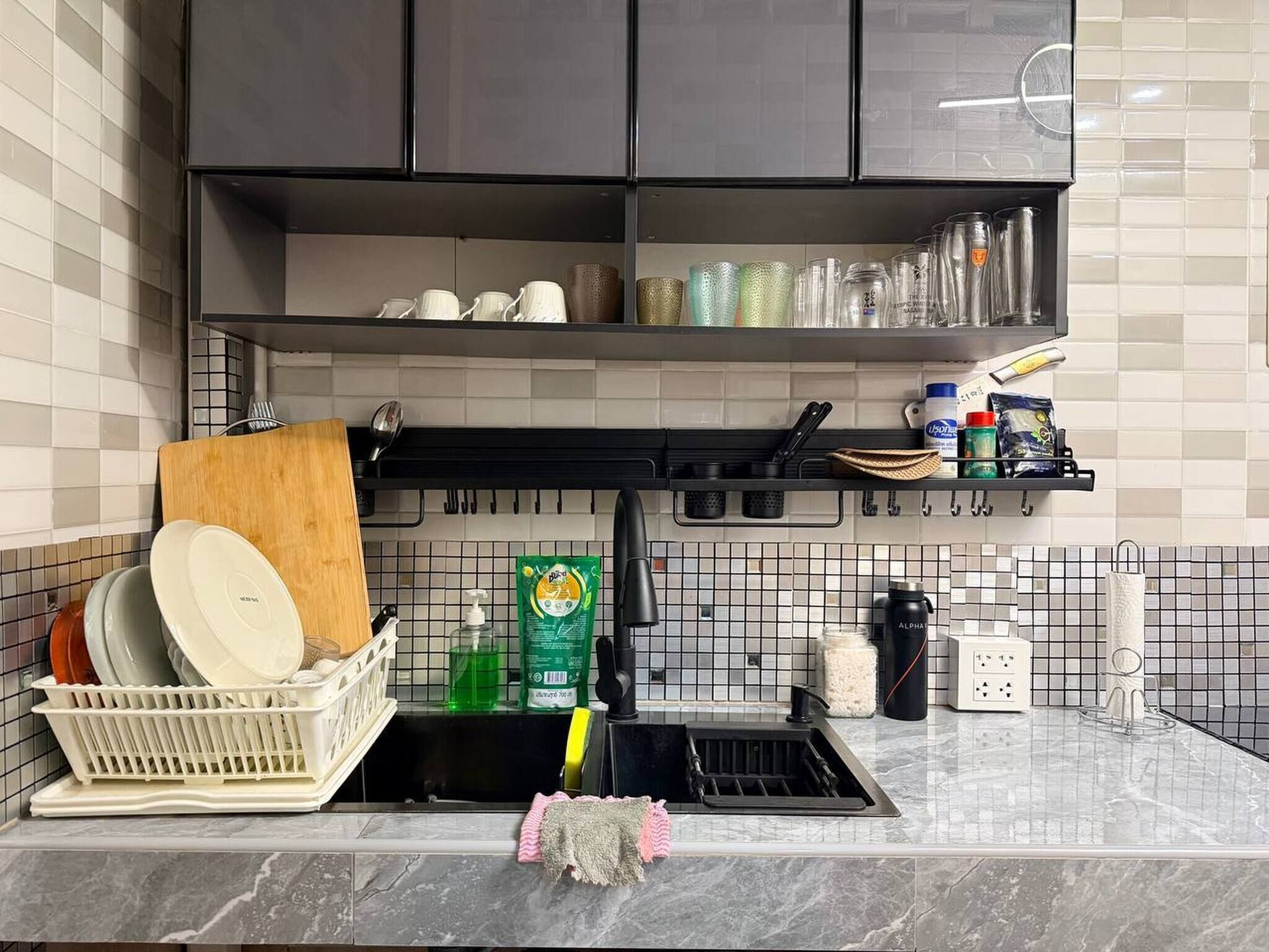 A kitchen with a dish rack, dish soap, a sponge, and a coffee maker.