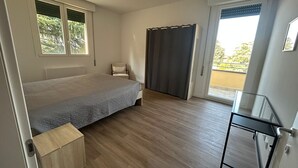 Een slaapkamer met een bed, een stoel, een bureau en een balkon.