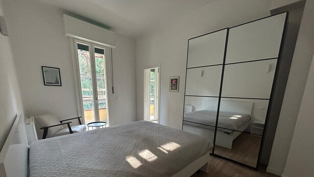 Um quarto com cama, uma cadeira, uma mesinha, uma porta de correr e um espelho grande.