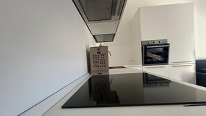 Uma cozinha moderna com bancada preta, forno embutido e painel elétrico fixado na parede.