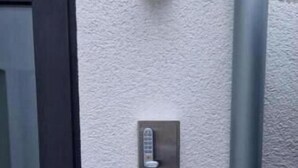 En dörr med ett lås, en väggmonterad intercom och ett grått rör.