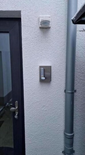Eine Tür mit Schloss, ein an der Wand montiertes Gegensprechanlage und eine graue Leitung.