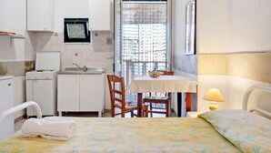 A compact room with a bed, a small table, a chair, a window with a curtain, a sink, and a stove. - Atenaion Studio Residence Holiday Home with Shared Terrace, Wi-Fi and Air Conditioning (Otranto)