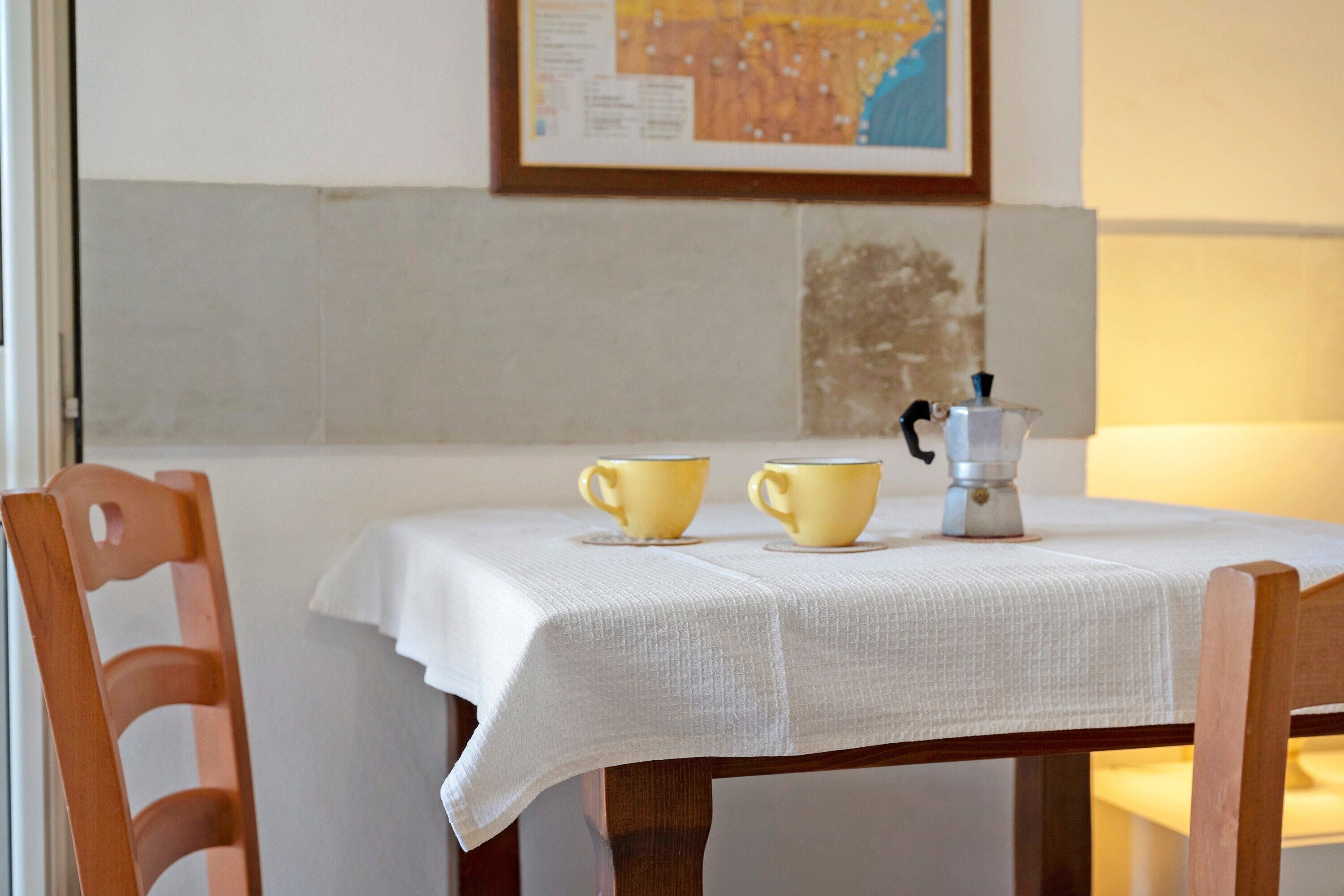 A table with a white tablecloth, two yellow cups, and a coffee pot.