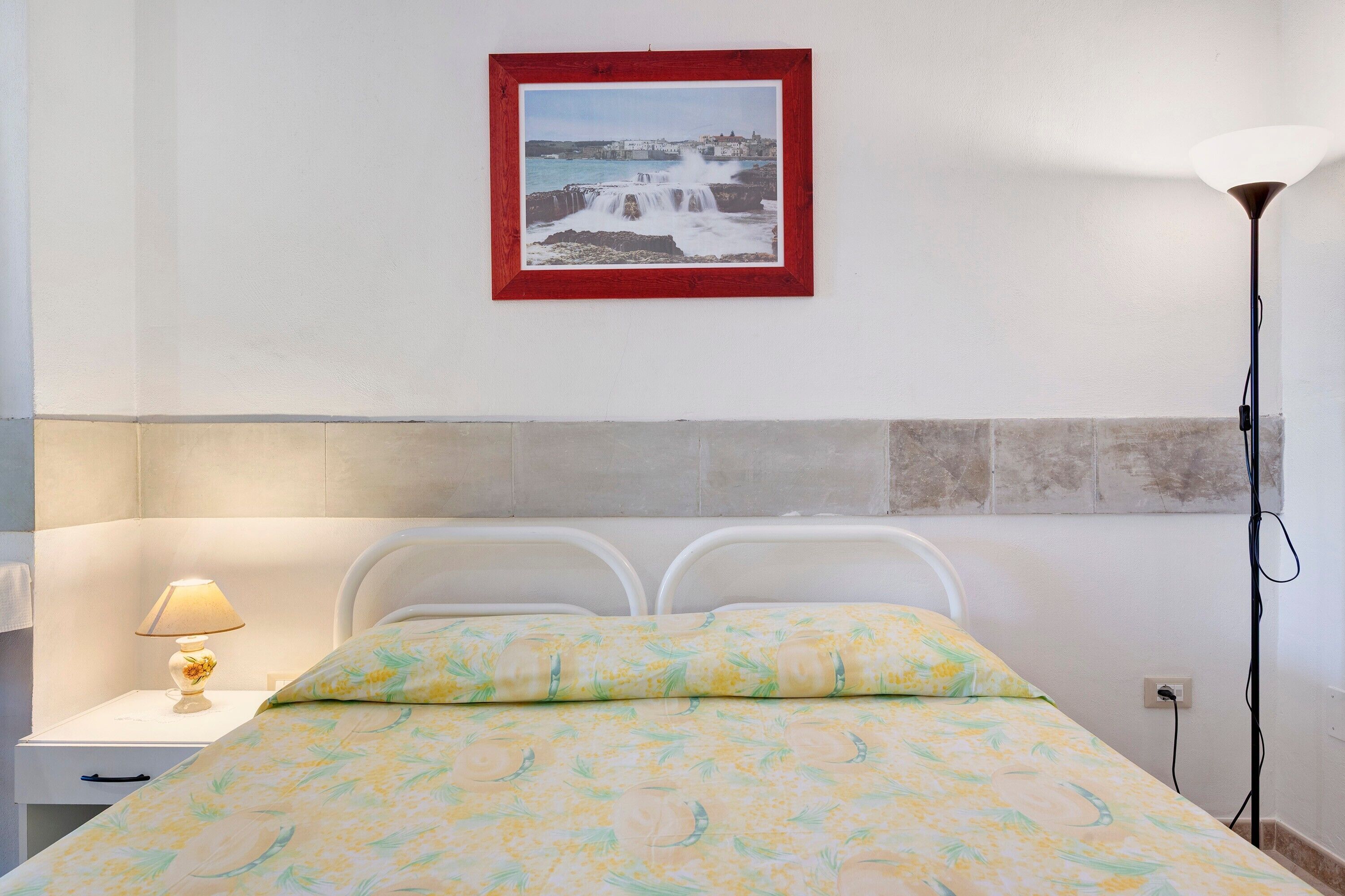 A bedroom with a bed, a nightstand, a lamp, and a framed picture on the wall.