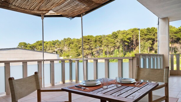 A wooden table set for two with chairs, a woven table mat, and a view of a forested hillside. - Atenaion Studio Residence Holiday Home with Shared Terrace, Wi-Fi and Air Conditioning (Otranto)